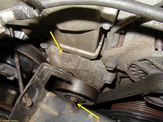 Idler pulley for serpentine belt. Upper arrow shows the tension adjuster; lower arrow is nut on idler pulley that must be looseneed to adjust tension.